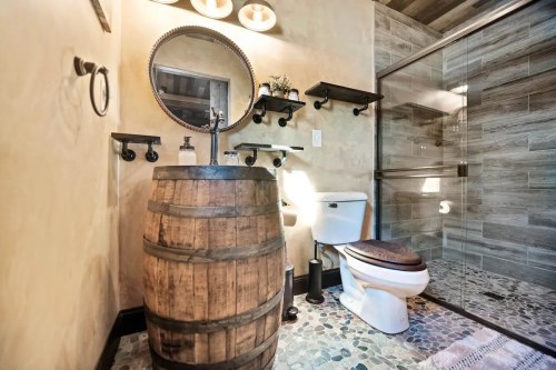 A rustic bathroom featuring a barrel sink, modern shower, and decorative shelves against a textured wall.