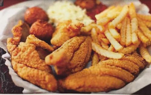 A plate of crispy fried fish fillets, crinkle-cut fries, hushpuppies, and coleslaw.