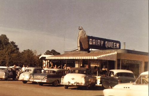 A vintage Dairy Queen with classic cars parked outside, people enjoying ice cream on a sunny day.
