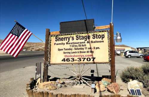 Sign for Sherry's Stage Stop, a family restaurant and saloon, with an American flag and contact information.