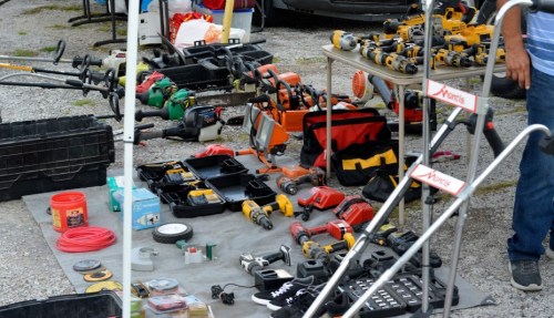 A variety of power tools and equipment displayed on a table and ground at a market or sale.