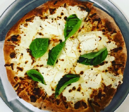 A freshly baked pizza topped with mozzarella cheese and fresh basil leaves on a metal tray.