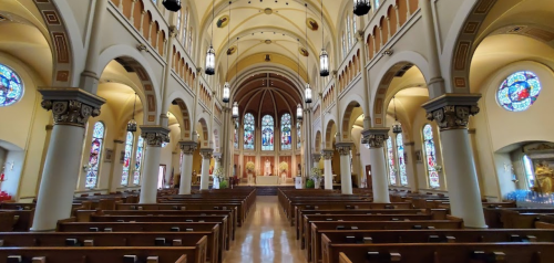 Interior of a grand church featuring arched ceilings, stained glass windows, and wooden pews.