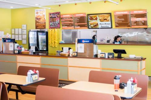 A bright diner interior with tables, a counter displaying menus, and a staff member behind the register.