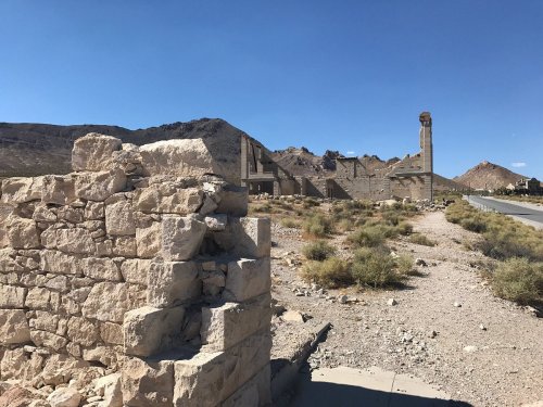 Ruins of a stone structure in a desert landscape, with mountains in the background under a clear blue sky.