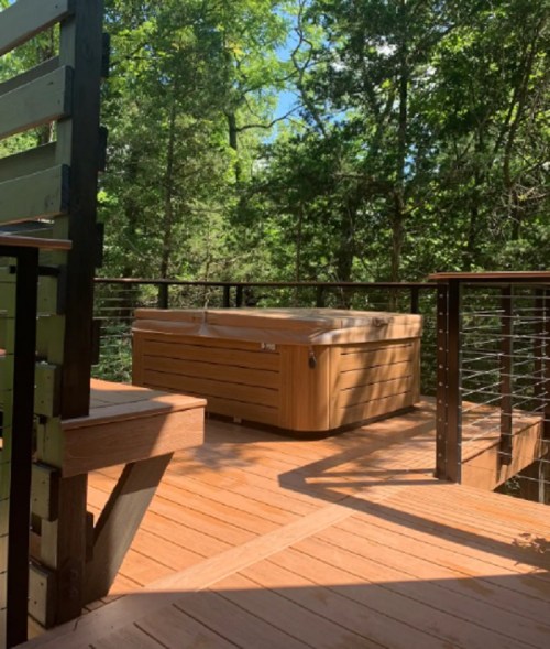 A wooden deck with a hot tub surrounded by lush green trees.