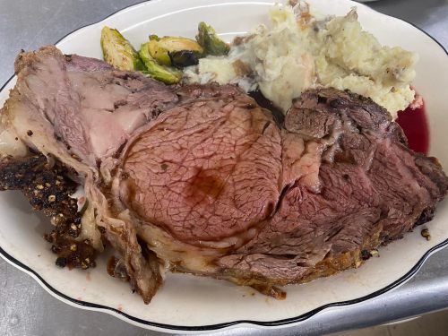 A large slice of prime rib served with mashed potatoes and Brussels sprouts on a white plate.