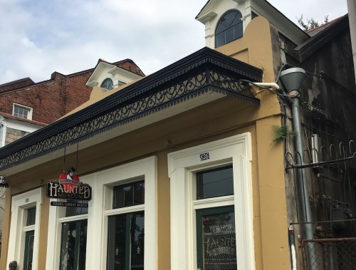 Exterior of a haunted museum with a sign, featuring a decorative roof and nearby buildings in a historic area.