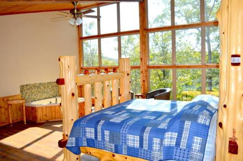 Cozy room with large windows, wooden furniture, and a blue patterned bedspread, overlooking a natural landscape.