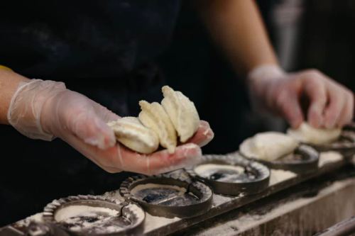 A person in gloves holds dumplings above a tray with flour-dusted molds.