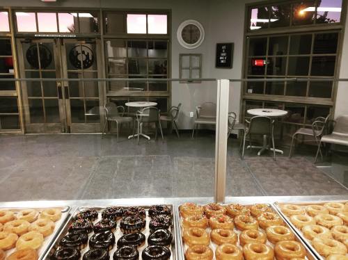 A display of assorted donuts in front of a cozy cafe with tables and large windows showing a sunset.