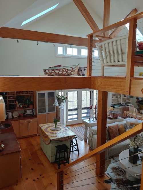 A spacious, modern interior with wooden beams, a loft area, and cozy furnishings in a bright, open layout.