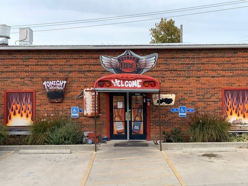 A brick building with a BBQ sign, welcoming entrance, and flame-themed decorations on the windows.