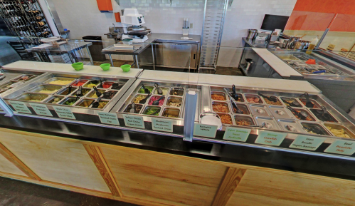 A vibrant salad bar with various toppings and ingredients in labeled containers, set in a modern restaurant.