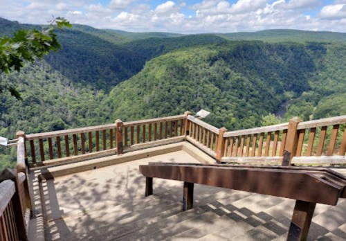 Scenic overlook with wooden railing, showcasing lush green hills and a valley under a partly cloudy sky.