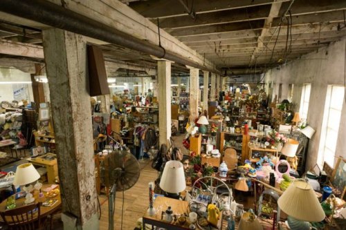 A spacious, cluttered antique shop filled with various items, furniture, and lamps under a rustic ceiling.