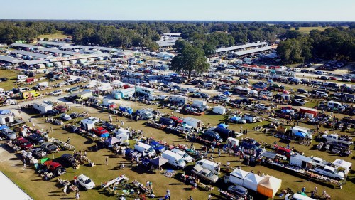 Aerial view of a bustling outdoor market with numerous tents, cars, and people enjoying the event.