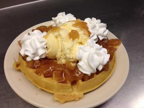 A waffle topped with vanilla ice cream, apple pie filling, and whipped cream, served on a plate.