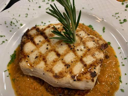 Grilled fish fillet garnished with rosemary, served on a bed of lentil sauce and sprinkled with herbs.