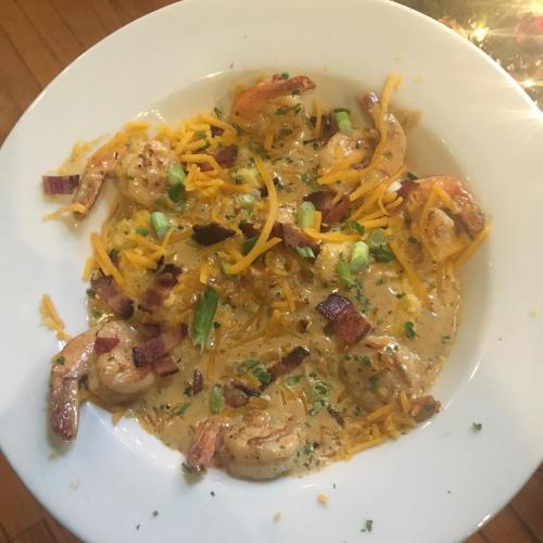 A bowl of creamy shrimp dish topped with cheese, bacon, and green onions, served on a white plate.