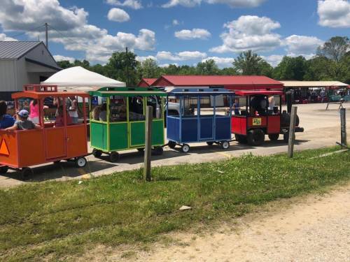 A colorful train ride with green, blue, orange, and red cars, parked in a sunny outdoor area with people nearby.