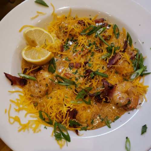 A bowl of shrimp pasta topped with shredded cheese, green onions, and lemon wedges.