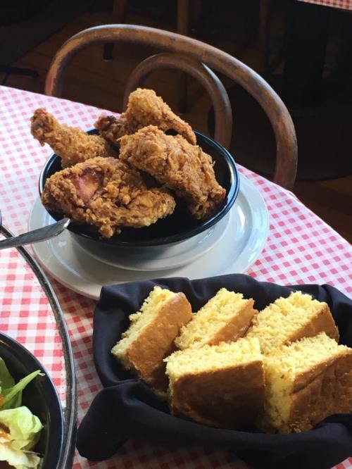 A bowl of crispy fried chicken next to a plate of golden cornbread on a checkered tablecloth.