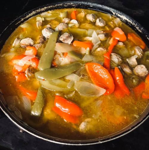 A pot of stew with meatballs, bell peppers, onions, and green beans simmering in a flavorful broth.