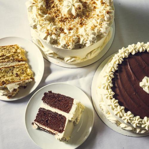 Three beautifully decorated cakes on a table, with a slice of chocolate cake on a plate in the foreground.