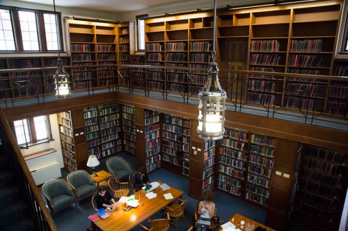 A spacious library with tall bookshelves, wooden tables, and people studying in a cozy, well-lit environment.