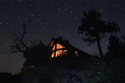 A cozy cabin illuminated at night, surrounded by trees under a starry sky.
