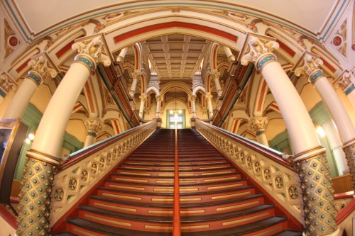 A grand staircase with ornate columns and colorful detailing, leading to a bright entrance at the top.