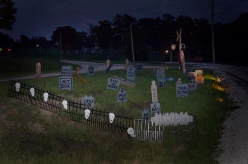 A spooky graveyard scene with tombstones, skulls, and eerie decorations, set near a road at night.