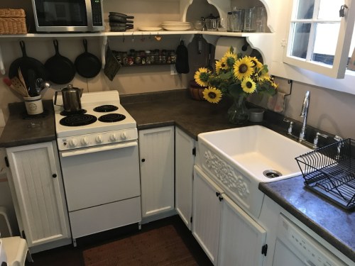A cozy kitchen with white cabinets, a stove, sink, and a vase of sunflowers on the counter.