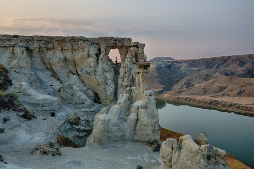 A scenic view of rugged white cliffs beside a calm river, with a hazy sky in the background.