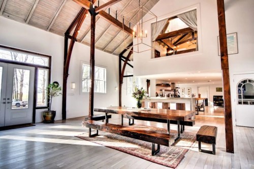 Spacious, modern interior with high ceilings, wooden beams, a large dining table, and a bright kitchen area.