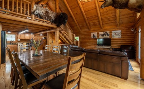 Cozy log cabin interior featuring a wooden dining table, leather sofa, and rustic decor with animal mounts.