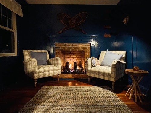 Cozy living room with two plaid armchairs, a warm fireplace, and a small side table on a textured rug.