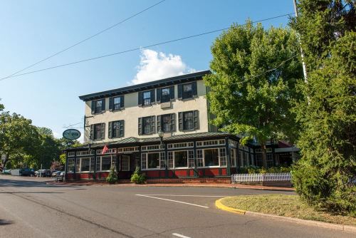 Historic building with green shutters and a porch, surrounded by trees and a clear blue sky.