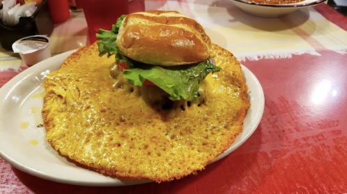 A large, cheesy crust surrounds a burger topped with lettuce and tomato, served on a white plate.