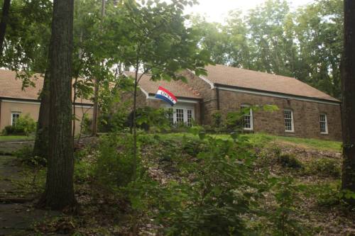 A stone building surrounded by trees, featuring a flag that reads "OPEN" in front.