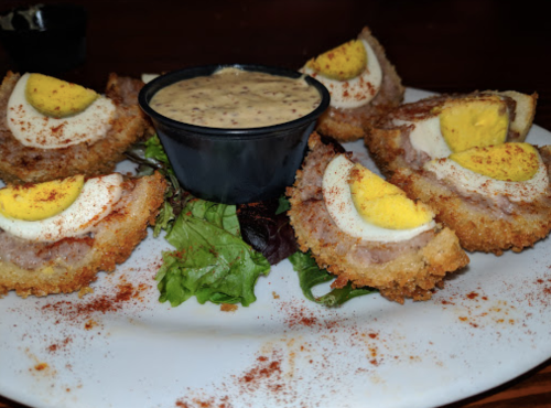 A plate of breaded and fried scotch eggs served with a dipping sauce and garnished with greens.