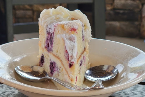 A slice of cake with layers of cream and berries, served on a plate with two spoons beside it.