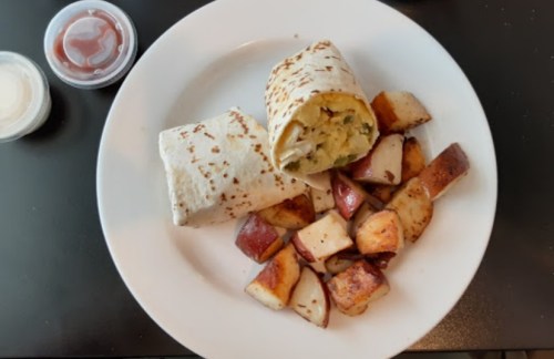 A plate with a wrapped burrito and diced, roasted red potatoes, accompanied by small containers of sauce.