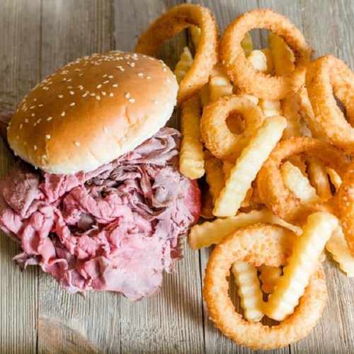 A sesame seed bun filled with sliced roast beef, accompanied by crispy onion rings and crinkle-cut fries.