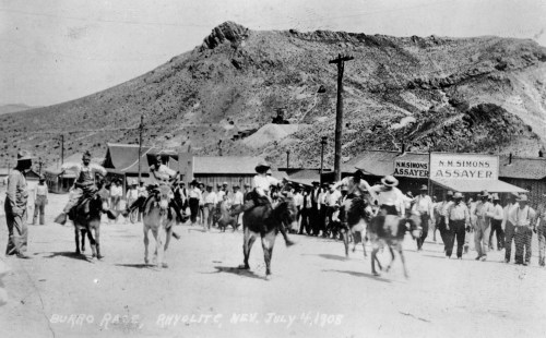 Historic black-and-white photo of a burro race in Rhyolite, Nevada, with riders and spectators on July 4, 1908.