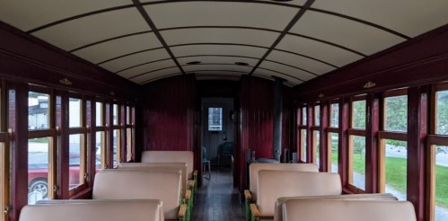 Interior of a vintage train car with wooden paneling and rows of beige seats, illuminated by natural light.