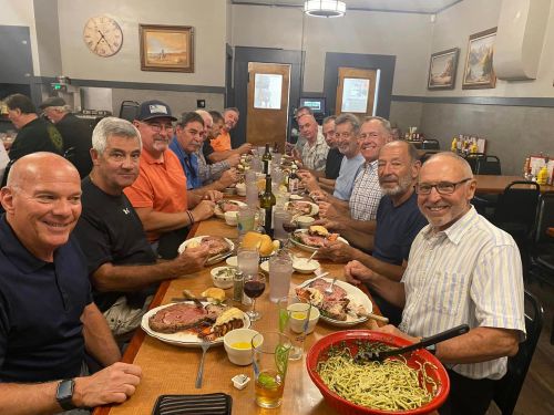 A group of men enjoying a meal together at a restaurant, featuring large plates of prime rib and side dishes.