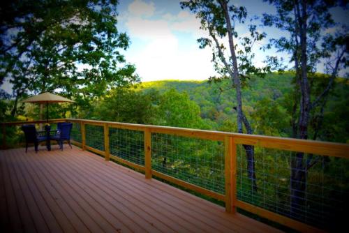 A wooden deck with two chairs and an umbrella overlooks a lush green landscape and distant hills.