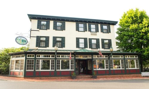 A charming three-story building with green shutters and red accents, featuring large windows and a welcoming entrance.